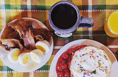 Delicious breakfast plates with pancakes, eggs, bacon and fruit with glass of orange juice and mug of coffee