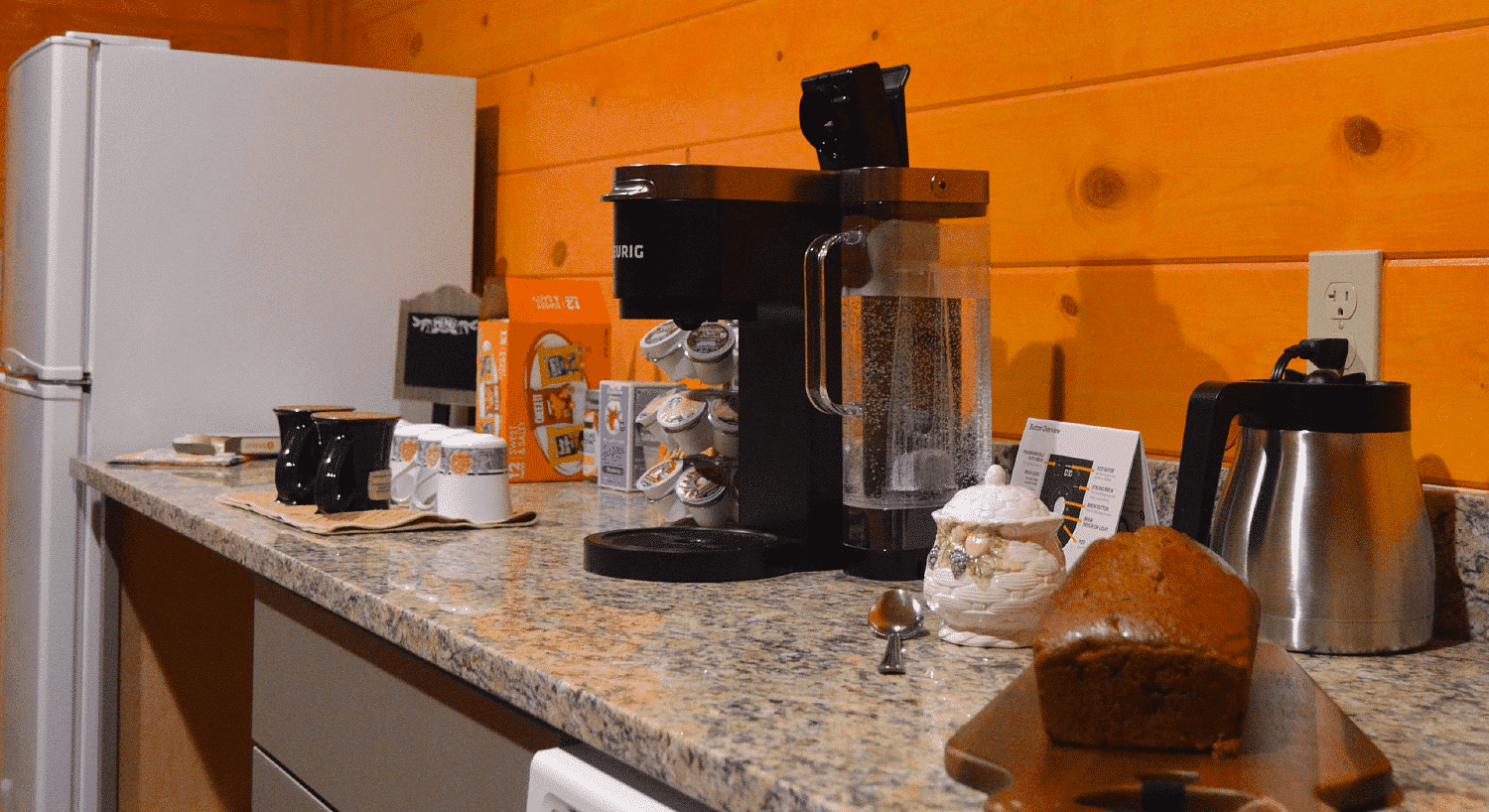 Kitchen counter with coffee maker, mugs, tea kettle and wooden board with a loaf of bread