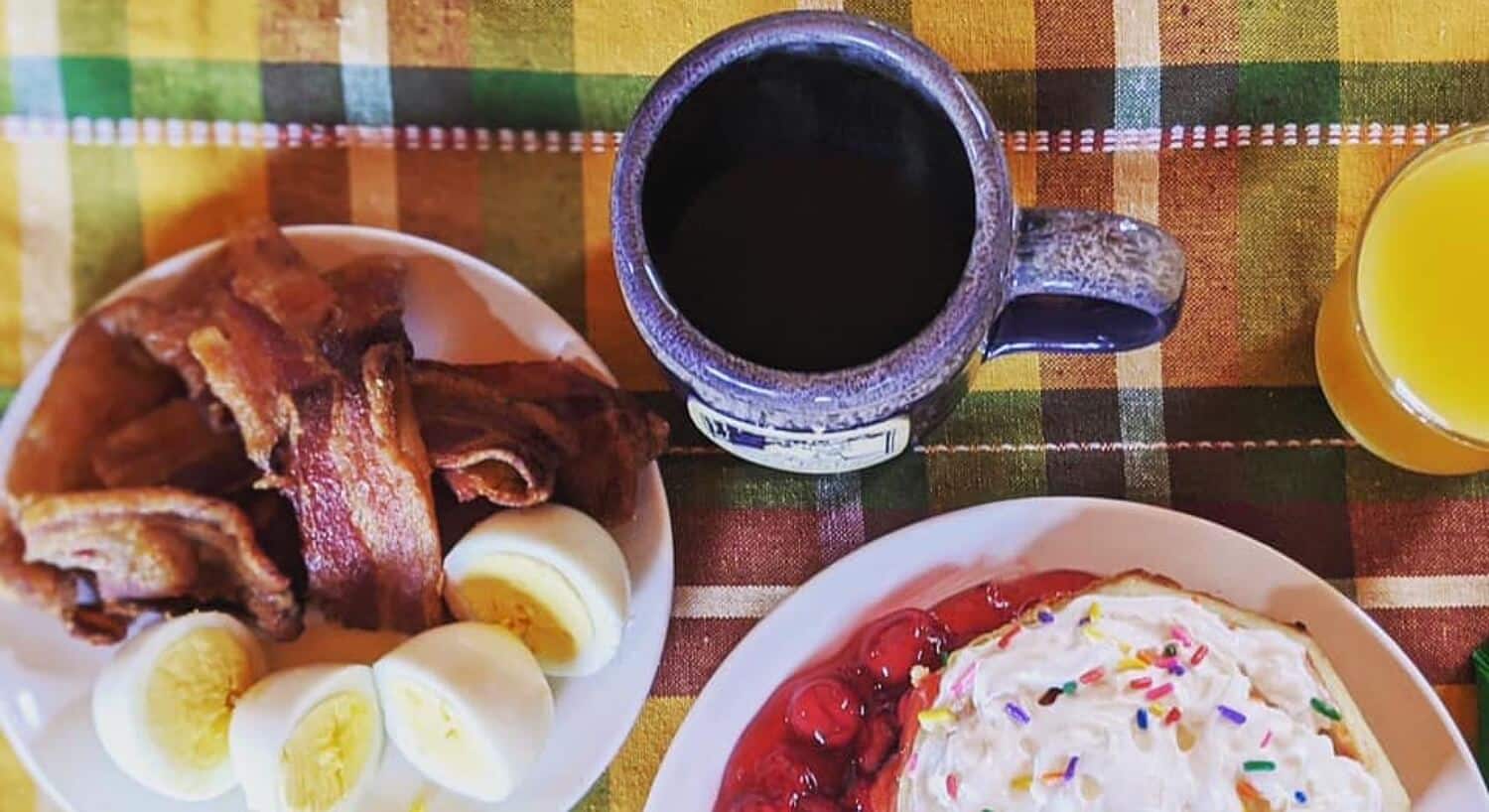 Delicious breakfast plates with pancakes, eggs, bacon and fruit with glass of orange juice and mug of coffee