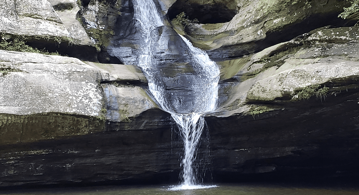 Large rocky cove with a waterfall cascading into a pool of water below