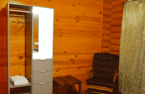 Log home bedroom with green curtains, sitting chair and small open closet with mirror