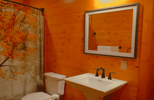 Log home bathroom with white pedestal sink, square mirror, toilet and stand up shower