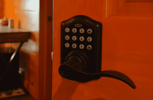 Black keypad door handle on a wooden door with writing desk in the background