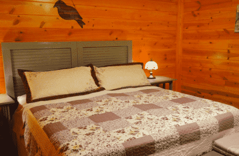 Log home bedroom with king bed, brown and cream quilt and bedside tables with lamps