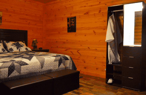 Bedroom in a log home with king bed, colorful quilt and small open closet with mirror and hanging white robe
