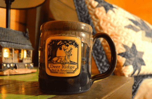 Blue ceramic mug with square business logo on a bedside table with a lamp