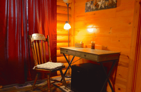 Writing desk with one wooden chair and floor lamp in bedroom with red curtains