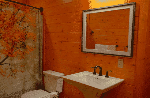 Bathroom of a log home with white pedestal sink, mirror, toilet and shower with curtain