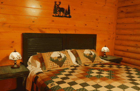 Bedroom in a log home with king bed, patchwork quilt, two bedside tables with lamps