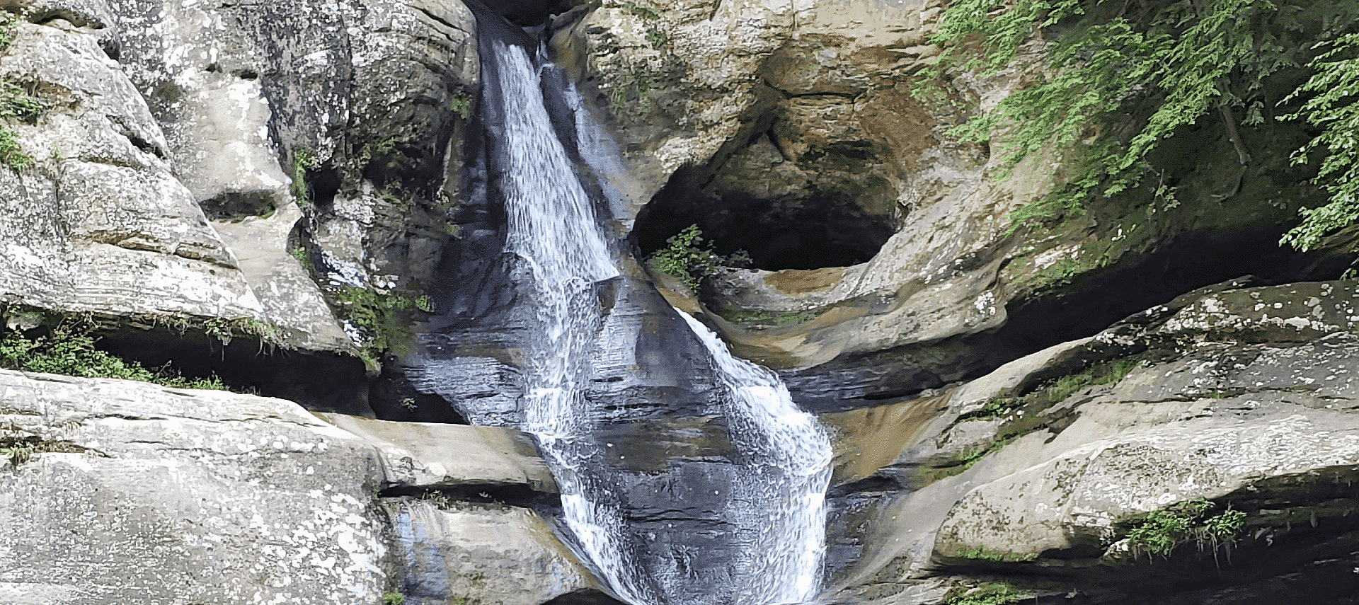 A cove of tall jagged rocks with a cascading waterfall and green trees