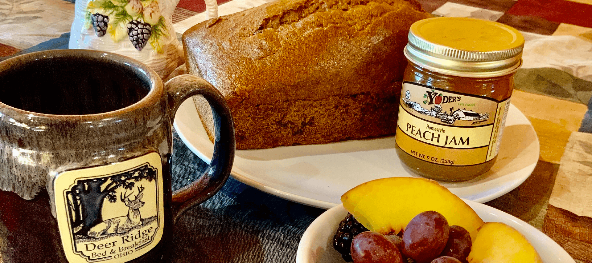 Plate with a loaf of bread and jam, bowl of mixed fruit and ceramic coffee mug