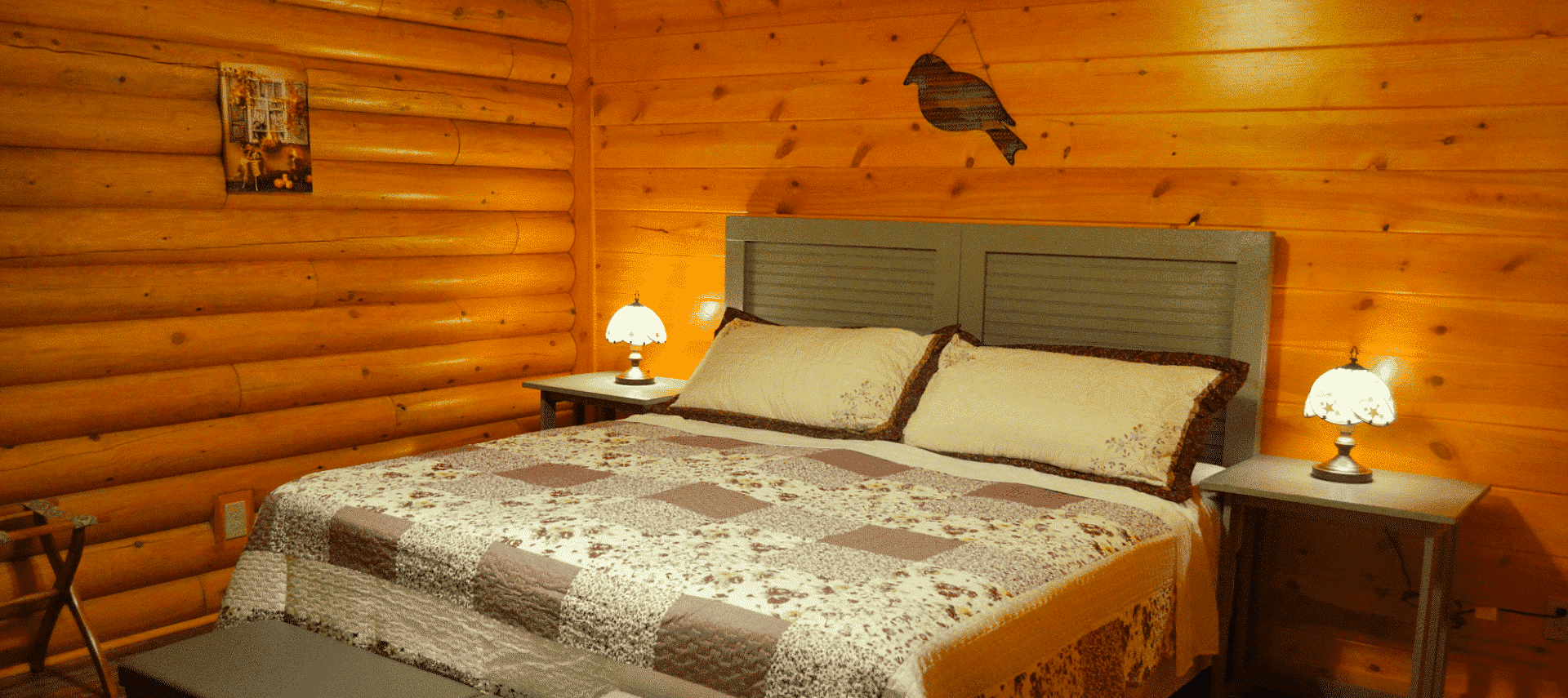 Log home bedroom with king bed, brown and cream quilt and bedside tables with lamps