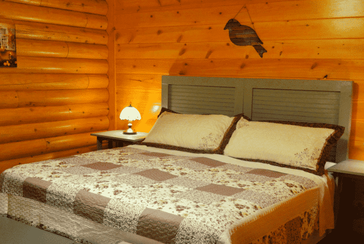 Log home bedroom with king bed, brown and cream quilt and bedside tables with lamps