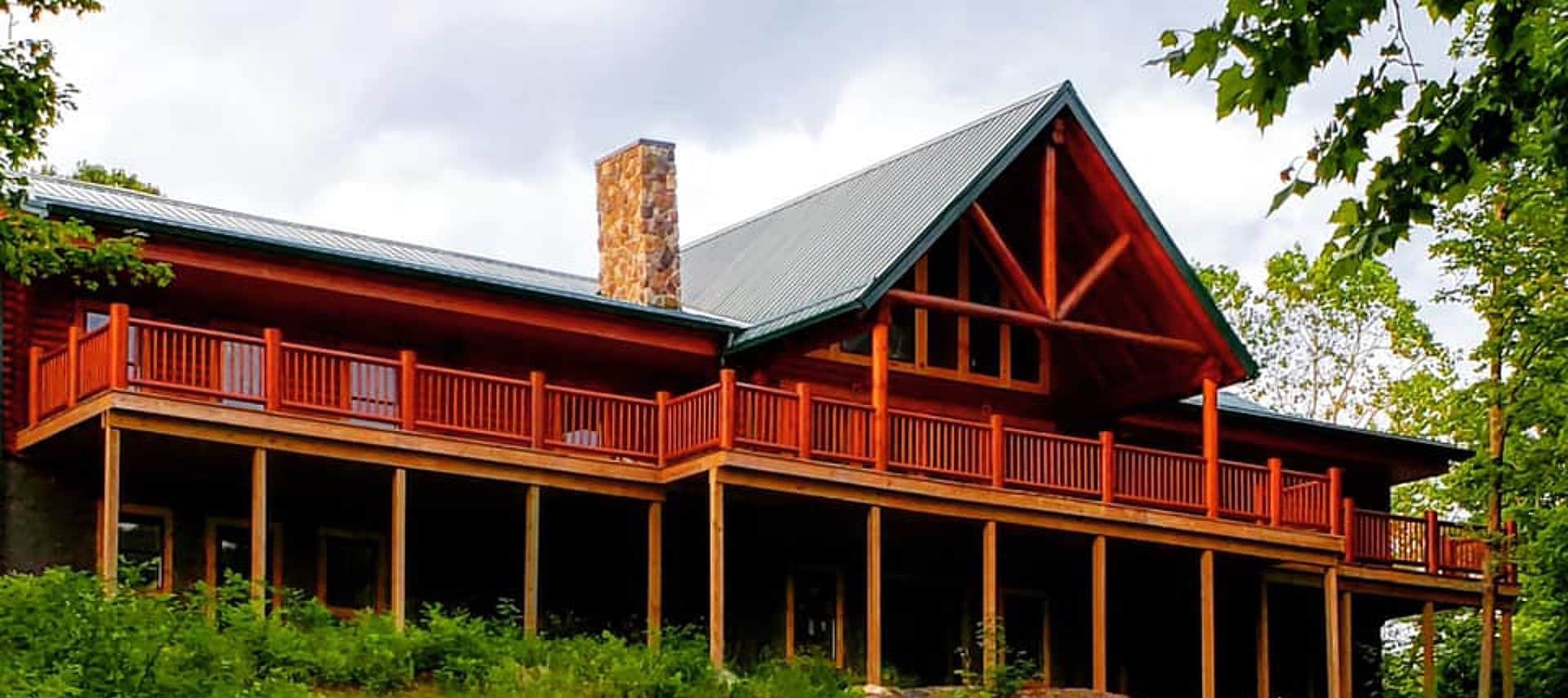 Front facade of large log home with expansive outdoor deck and green roof with stone chimney