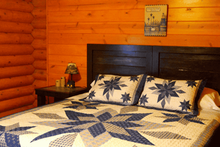 Bedroom in a log home with king bed, blue and white quilt and bedside tables with lamps