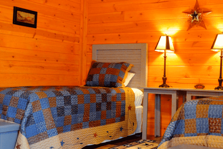 Two twin beds with beside tables and lamps in a log home bedroom with natural wood walls