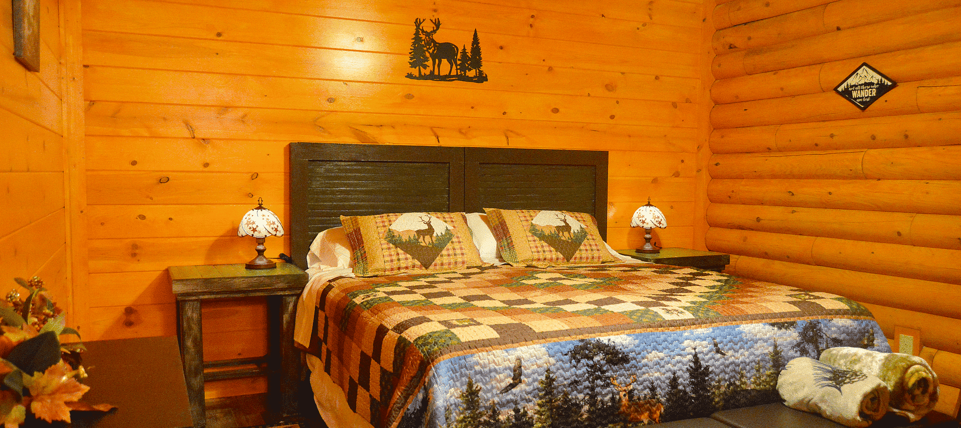 Bedroom in a log home with king bed, colorful quilt, and bedside tables with small tiffany lamps