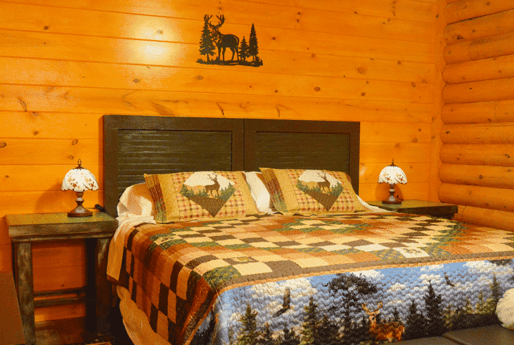 Bedroom in a log home with king bed, colorful quilt, and bedside tables with small tiffany lamps