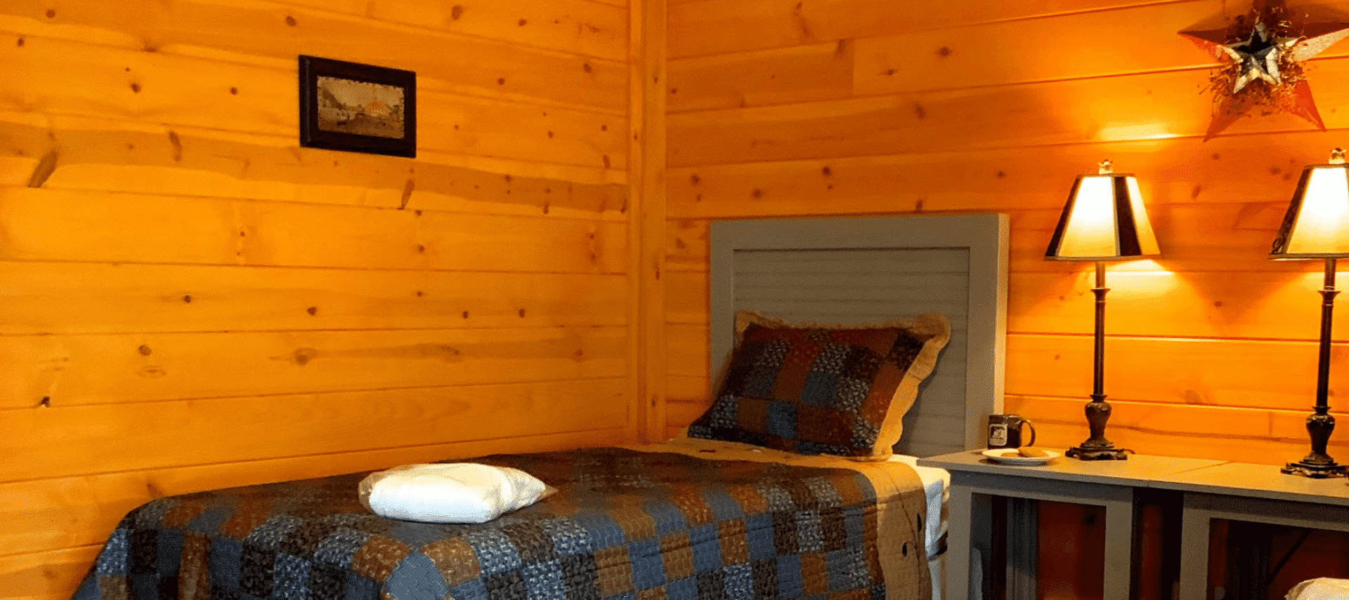 Bedroom in a log home with natural wood walls, twin bed with quilt and tall bedside lamps