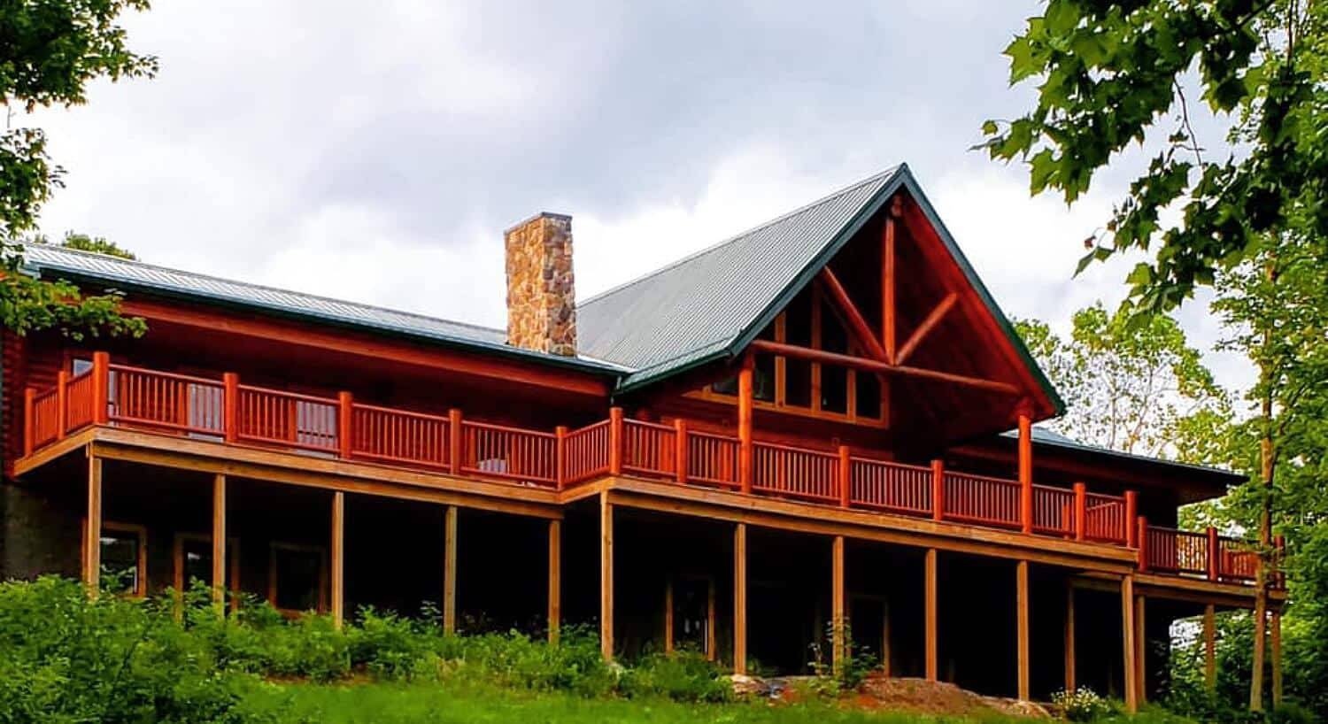 Front facade of large log home with expansive outdoor deck and green roof with stone chimney