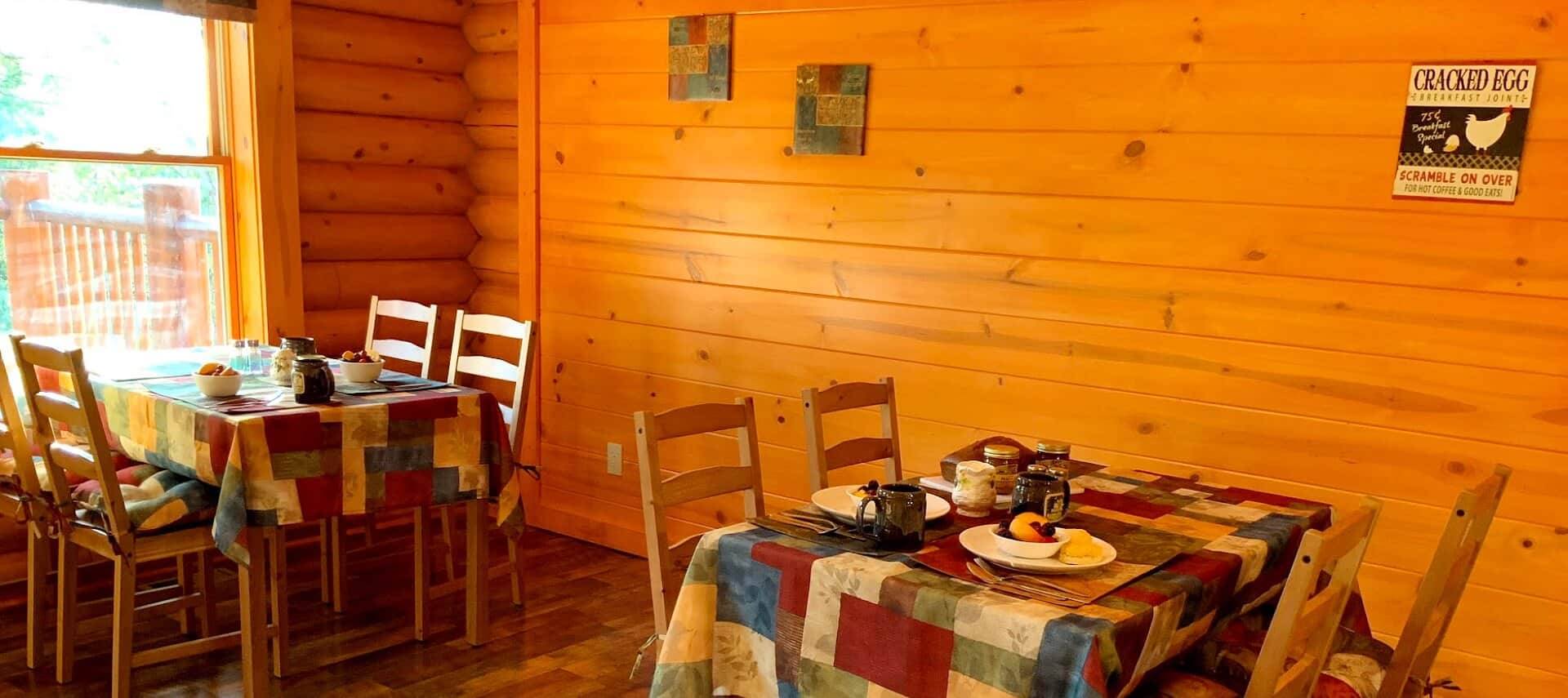 Dining area of a log home with two tables with four chairs and multicolored tablecloths