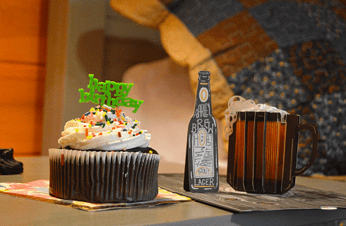 One chocolate cupcake with white frosting with a green happy birthday sign on a bedside table